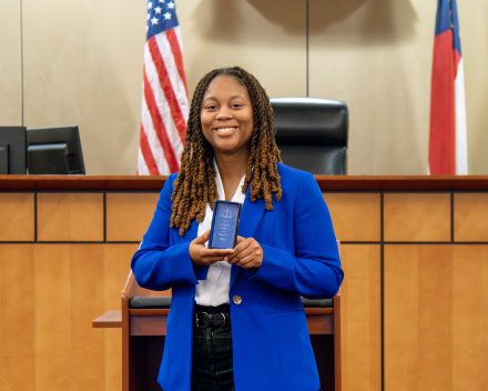 Kristian Ellis in a bright blue blazer, standing inside a courtroom smiling and holding an award plaque.