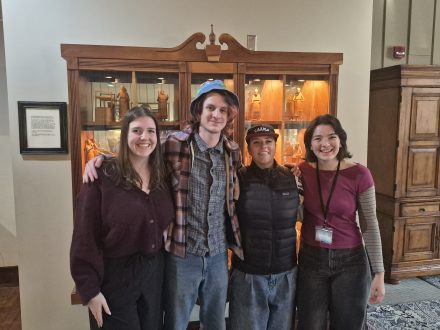 Four Elon students pose for a photo in front of a cabinet
