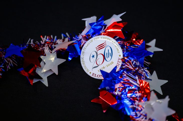 A festive button celebrating America’s 250th anniversary lies on a black surface with red, white, and blue star garland.