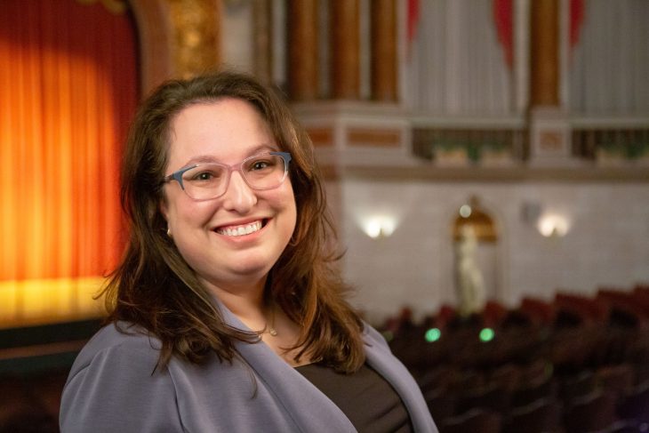 Attorney Blaire McClanahan pictured in a large theater. She is wearing a purple business suit and smiling warmly at the camera.