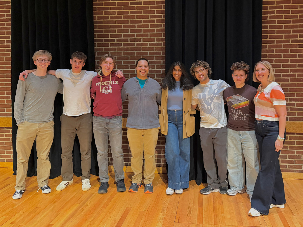 Eight people pose for a photo in a line in front of a brick wall