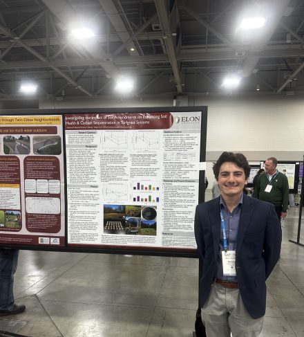 A young man stands beside a research poster board