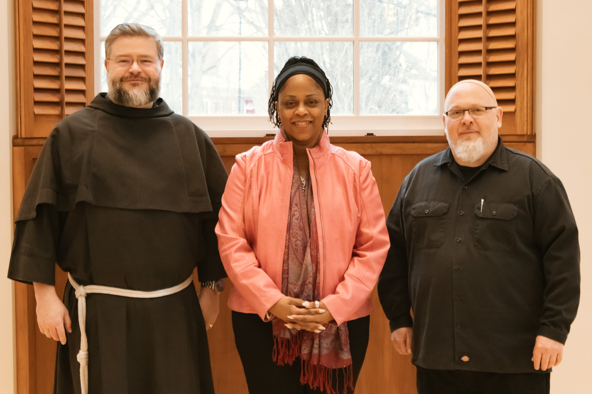 Three people stand next to each other for a photo in front of a window