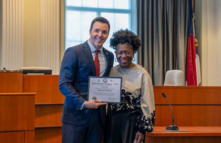 A woman and man stand together smiling, holding an award plaque.