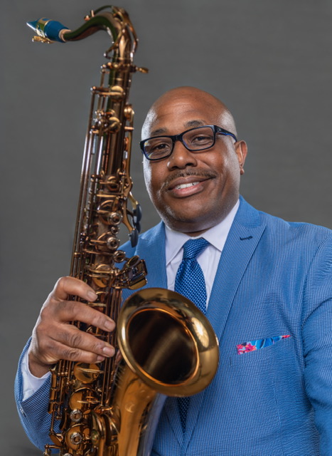 Photo of a man in a blue suit holding up a saxophone