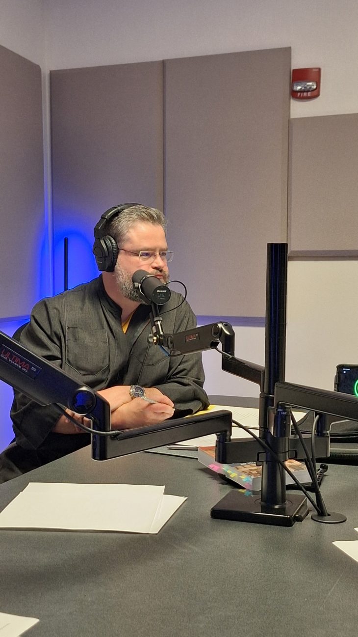 Man sitting at desk with podcast equipment in front of him.