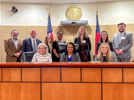 A group of 10 faculty and students behind the bench in the Robert E. Long Courtroom at Elon Law.