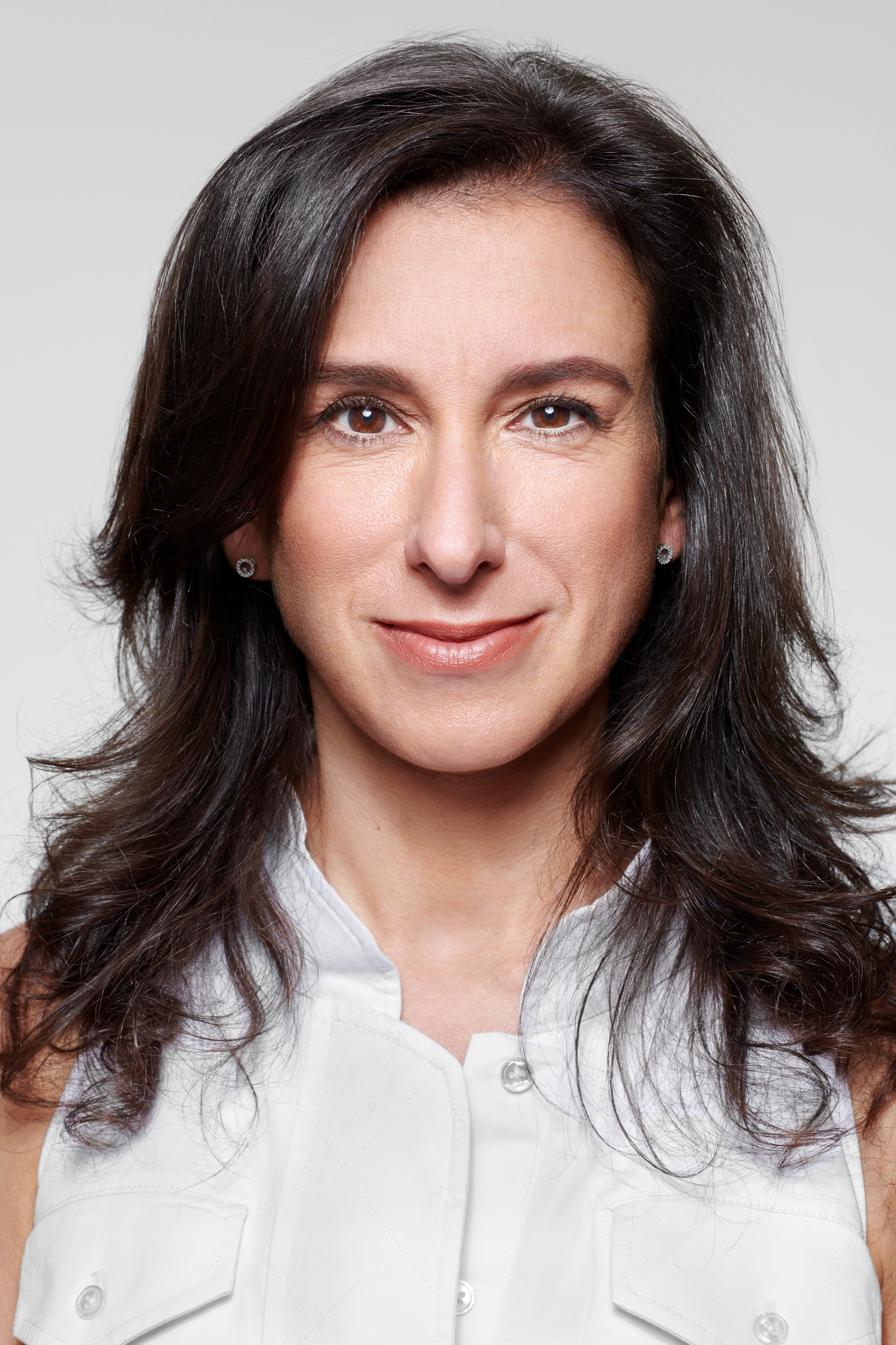 A headshot of Jodi Kantor smiling into the camera. She has dark brown hair and is wearing a white shirt
