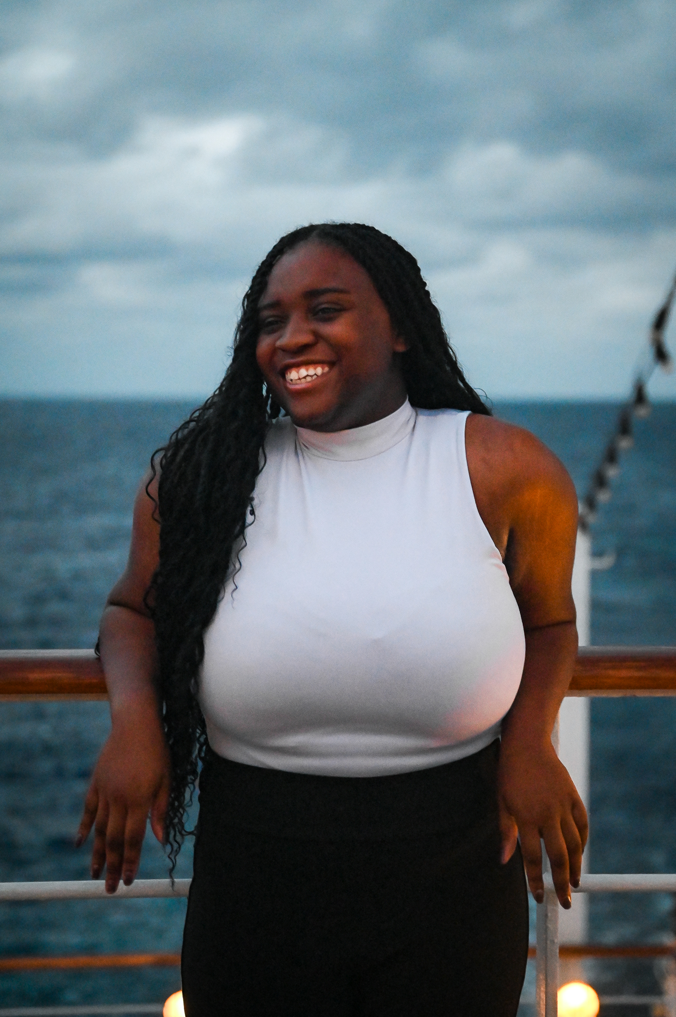 A woman stands on a boat deck smiling in a white sleeveless top