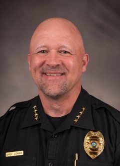 Joe LeMire wears a black officer uniform with four stars on each collar, a name tag and a police badge.