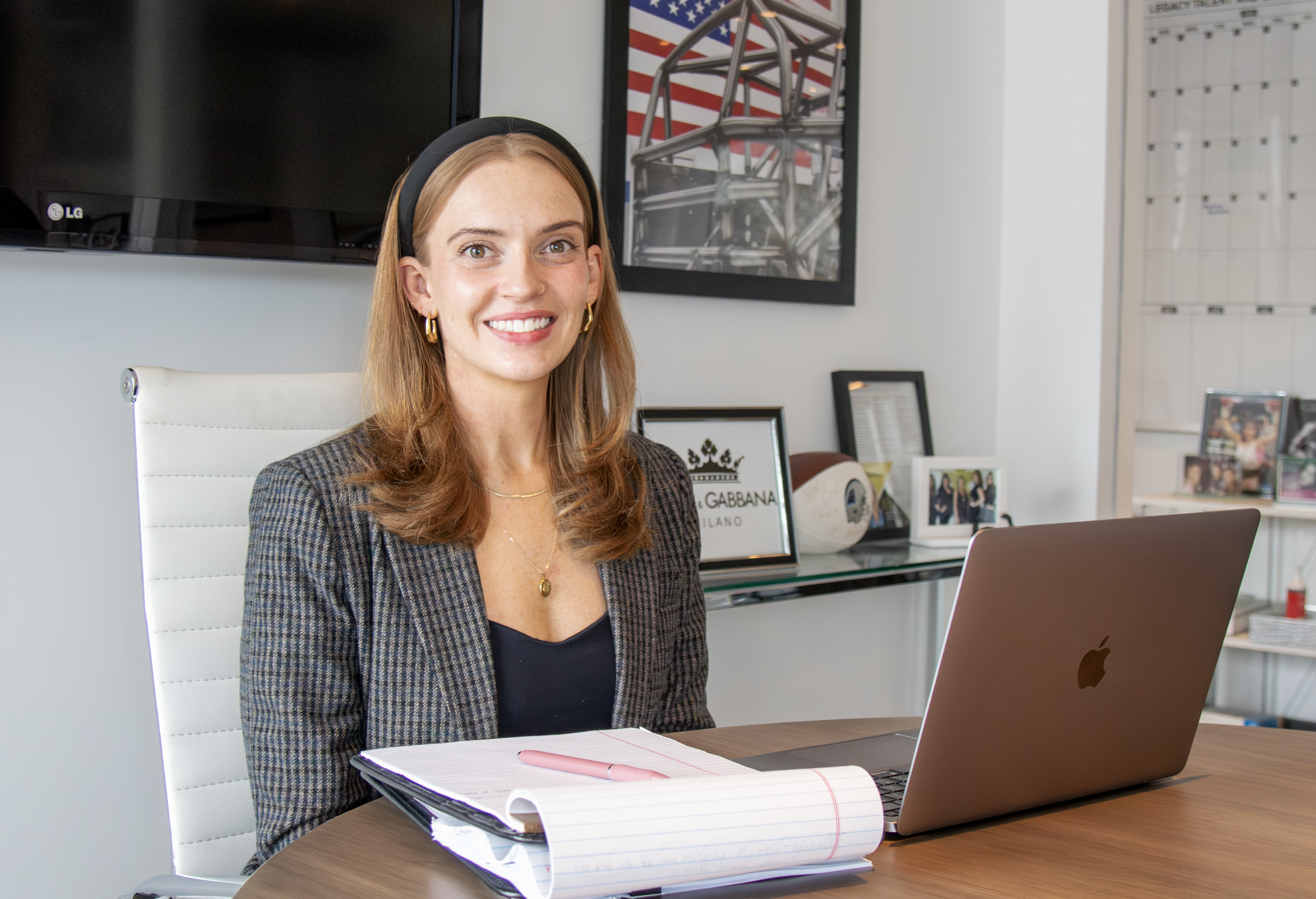 A woman at a conference room table with a laptop computer and legal pad. She is smiling at the camera.