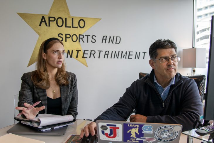 A woman and man look intently at a monitor screen. She is speaking and gesturing. Apollo Sports and Entertainment" is painted on the wall behind them.