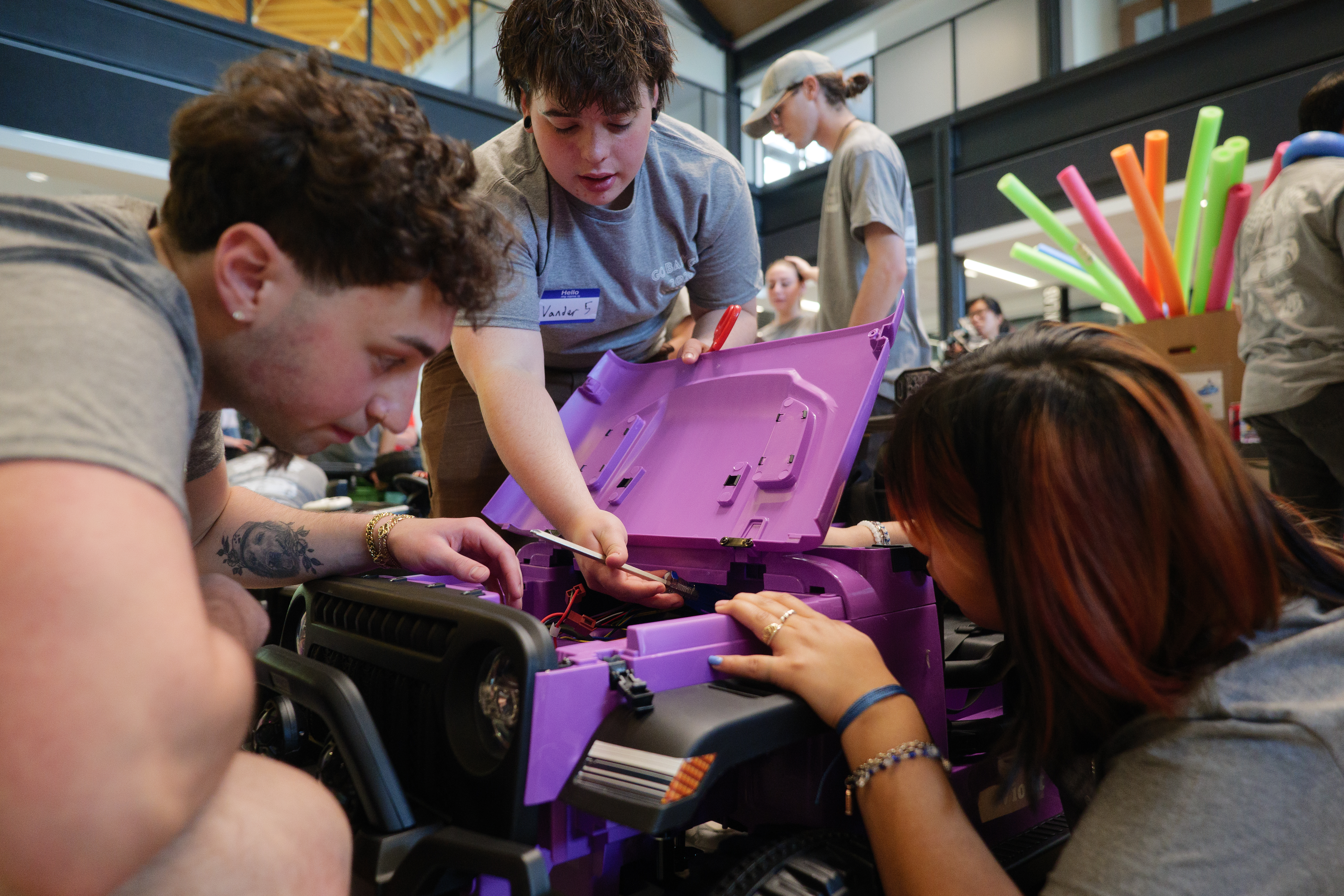 Students work together to repair wiring inside a purple ride-on toy car during a hands-on workshop.