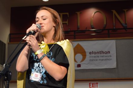 Nikki Sanz '18, singing with a microphone in hand, wearing black.