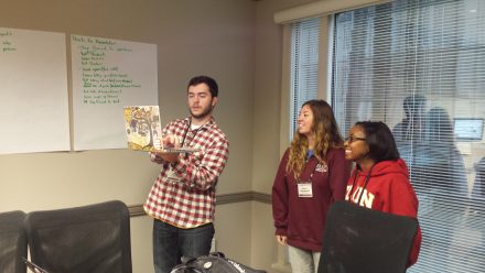 Jensen Roll '16 seen holding a laptop with two students in a study room.