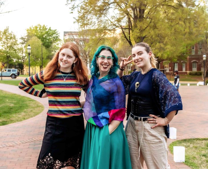 Three friends pose together outdoors on a brick pathway, smiling at the camera.