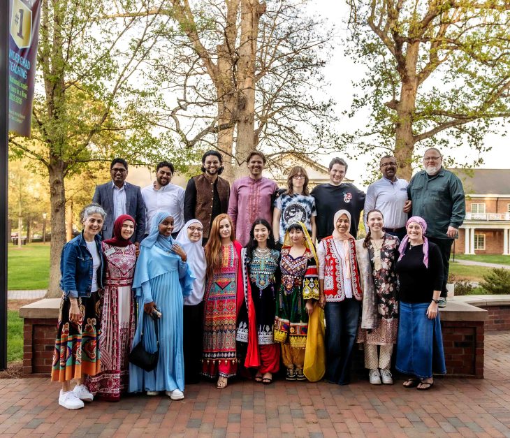 A large group of people in colorful traditional and casual outfits pose together outdoors.