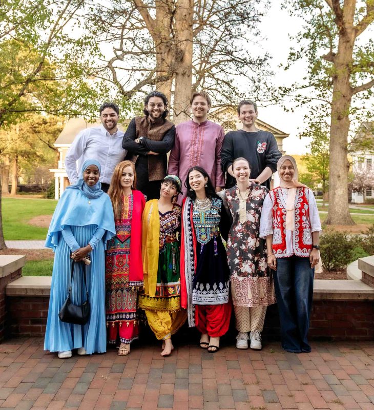A large group of people in colorful traditional and casual outfits pose together outdoors.