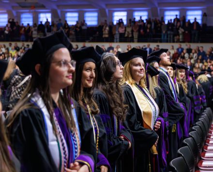 A group of law school graduates smile hopefully in academic regalia inside Alumni Gym.