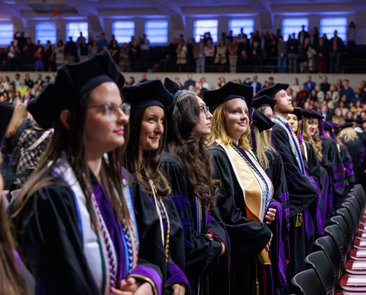 A group of law school graduates smile hopefully in academic regalia inside Alumni Gym.
