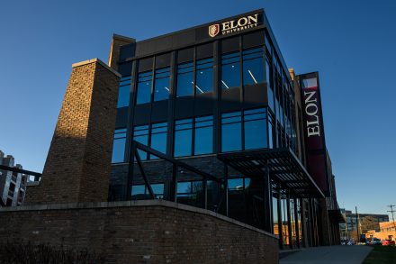 The exterior of an Elon University building in Charlotte, featuring large glass windows and an “Elon” sign on the facade.