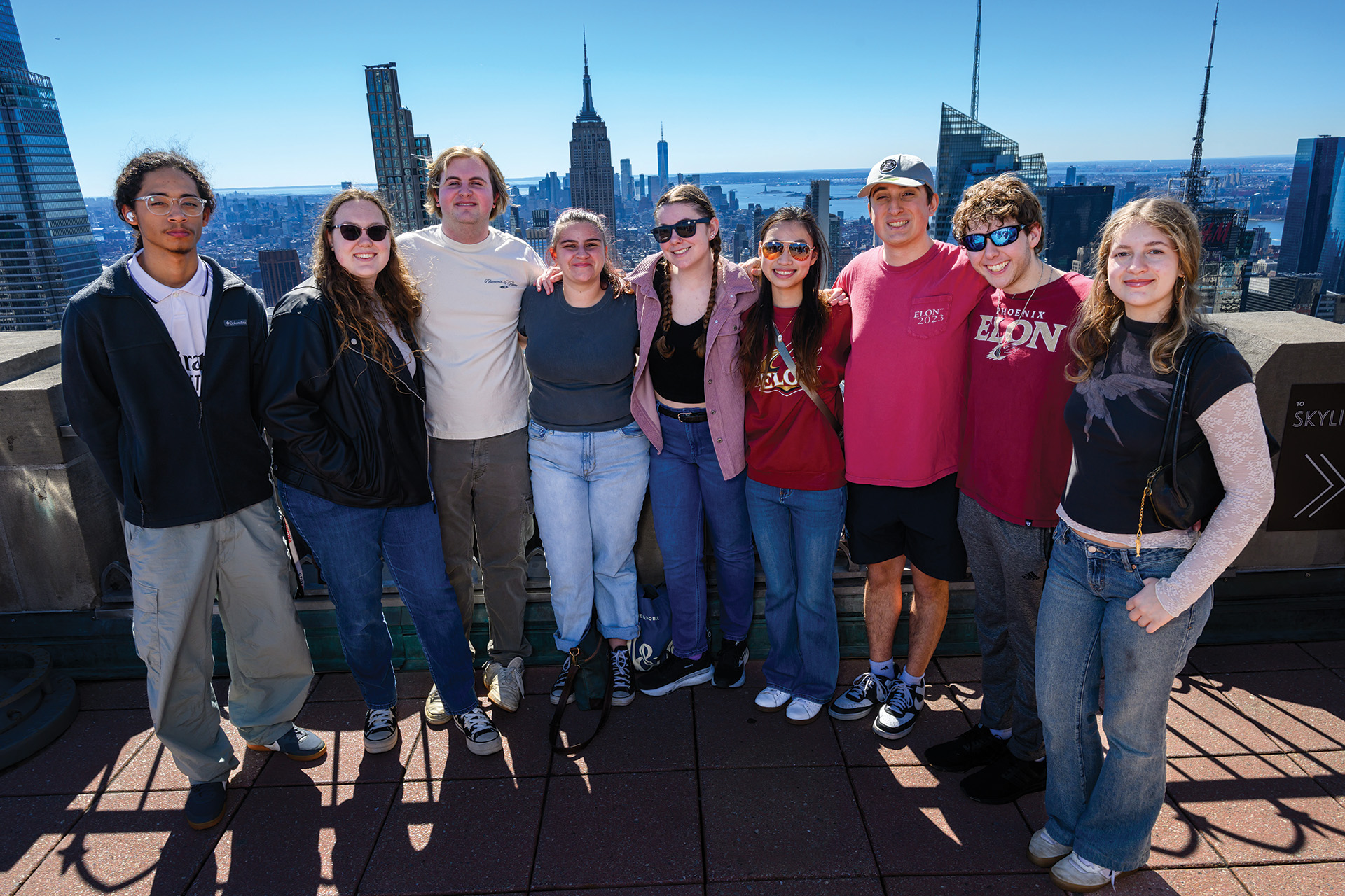A group of students pose together on a rooftop observation deck with the New York City skyline in the background.