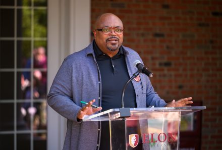 Dean of Elon College, the College of Arts and Sciences Hilton Kelly wearing a black polo with a grey jacket standing at the podium giving remarks to celebrate 30 years of the International & Global Studies program.