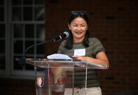Emily Ecker ’26 wearing a green top standing at the podium giving tributes to the International & Global Studies program.