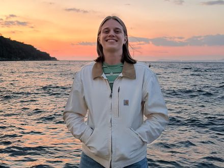 Phot of Catherine Dierker in a white jacker posing for a photo in front of water