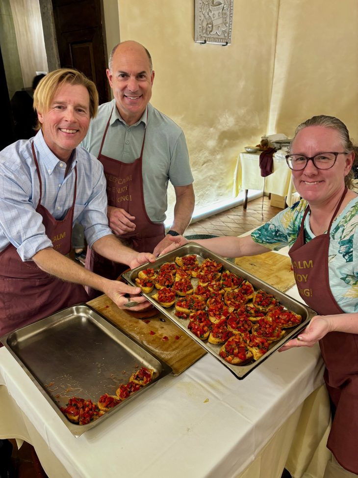 Three people in aprons smile to the camera while holding a tray of food