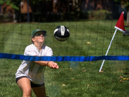 A faculty/staff member bumps a volleyball over the net during a game on the lawn, focused on the ball mid-play.