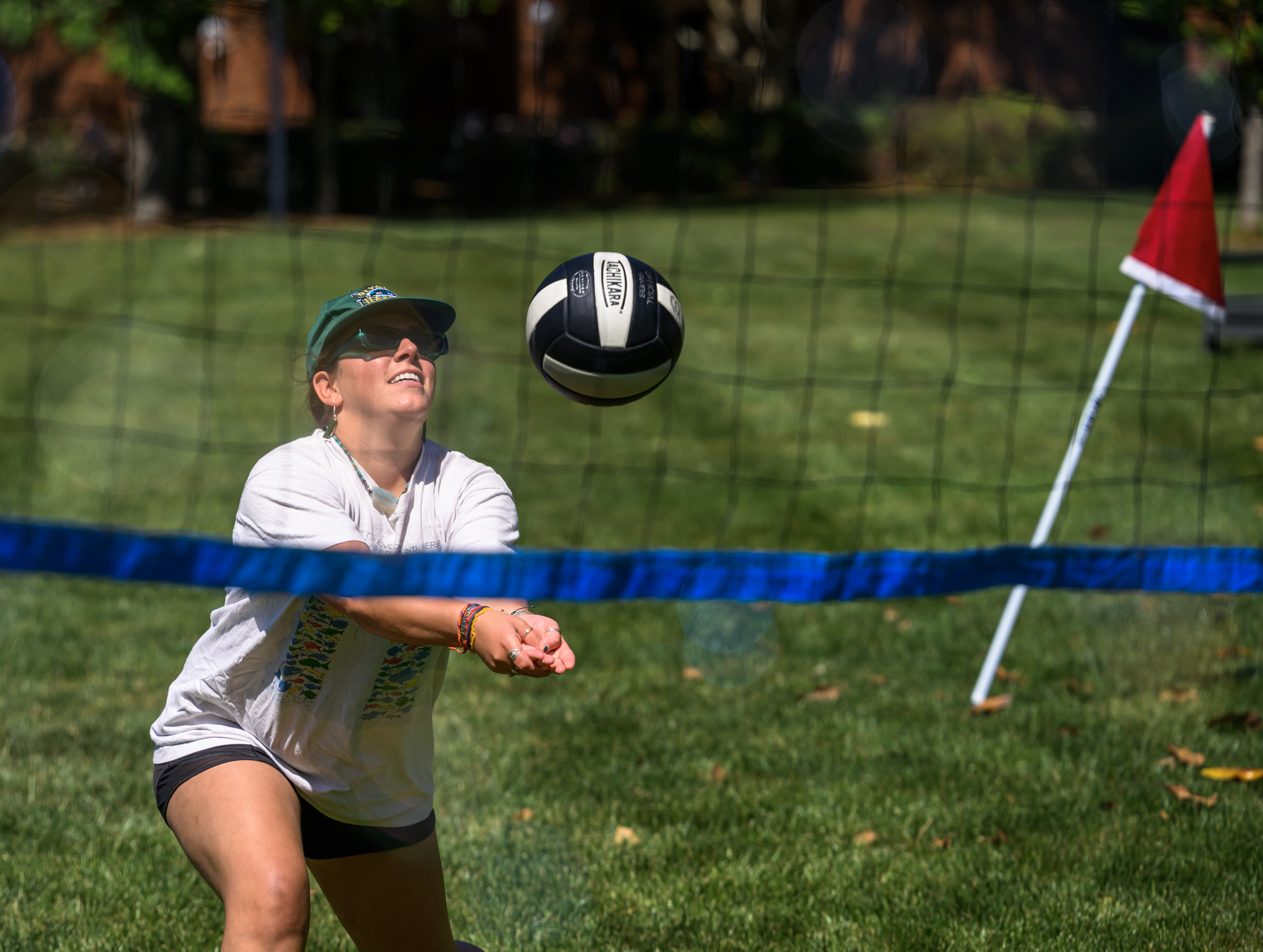 A faculty/staff member bumps a volleyball over the net during a game on the lawn, focused on the ball mid-play.