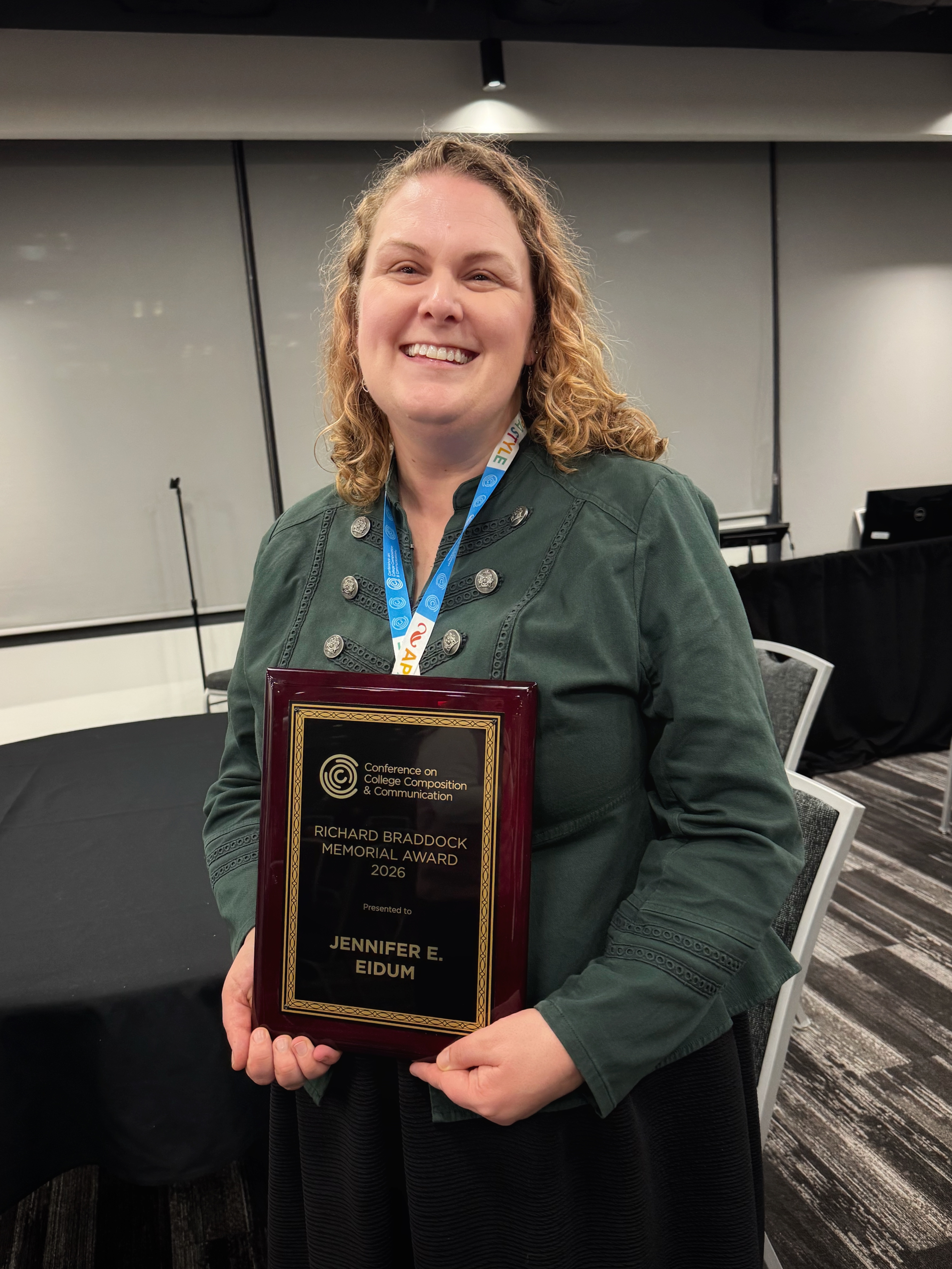 Jennifer Eidum is wearing a green blouse and and is holding the plaque she received for the CCCC Richard Braddock Award.