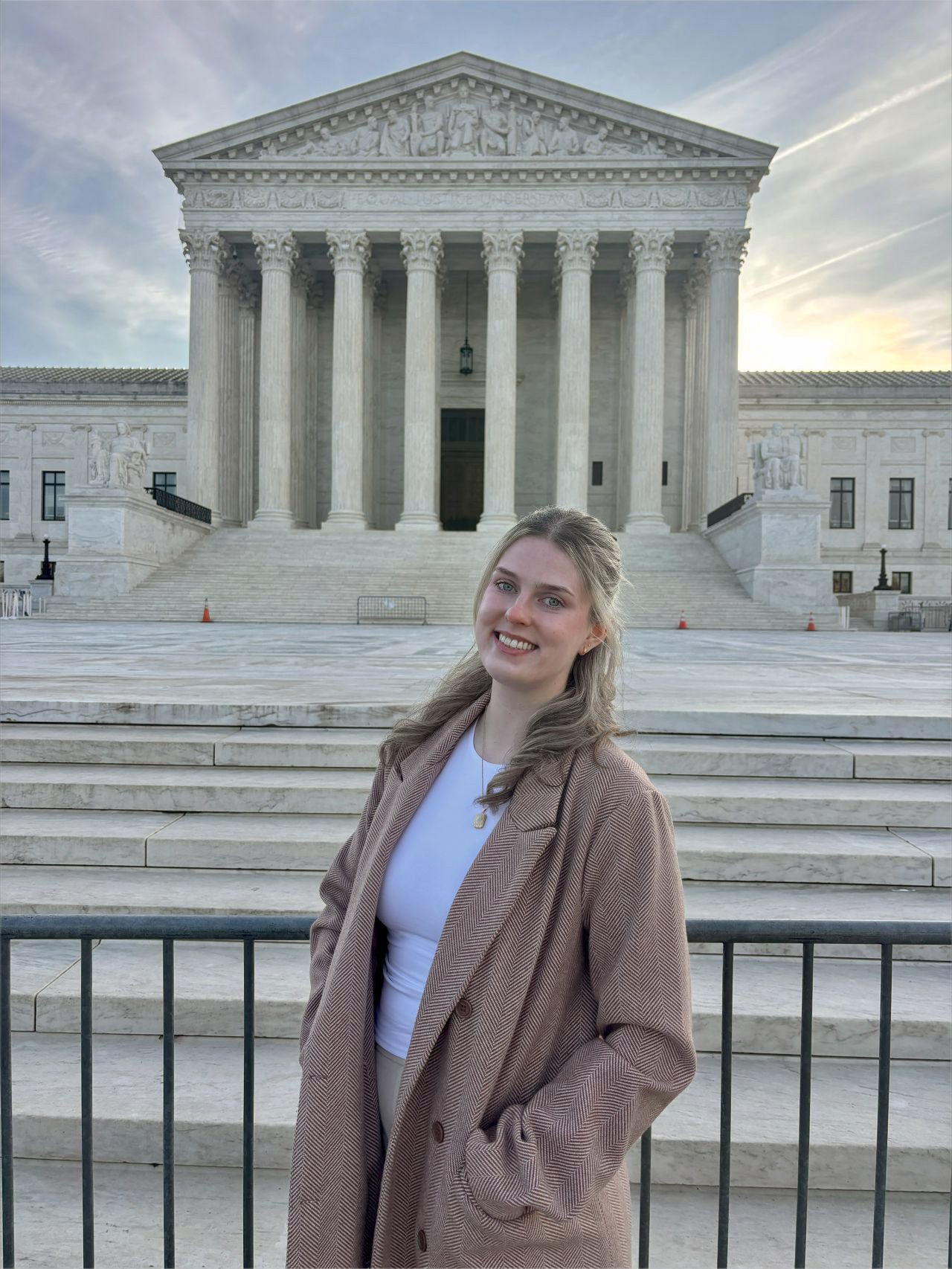 Isabel Craige in front of the U.S. Supreme Court building at dawn. She is smiling standing at the steps, showing the columns and entrance in the background.