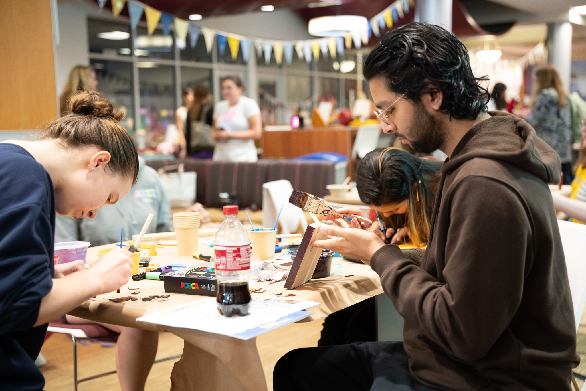students sitting at a table in the mosely student center painting wooden blocks