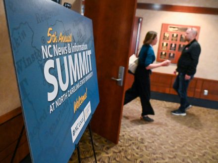 Attendees walk by a Summit poster.