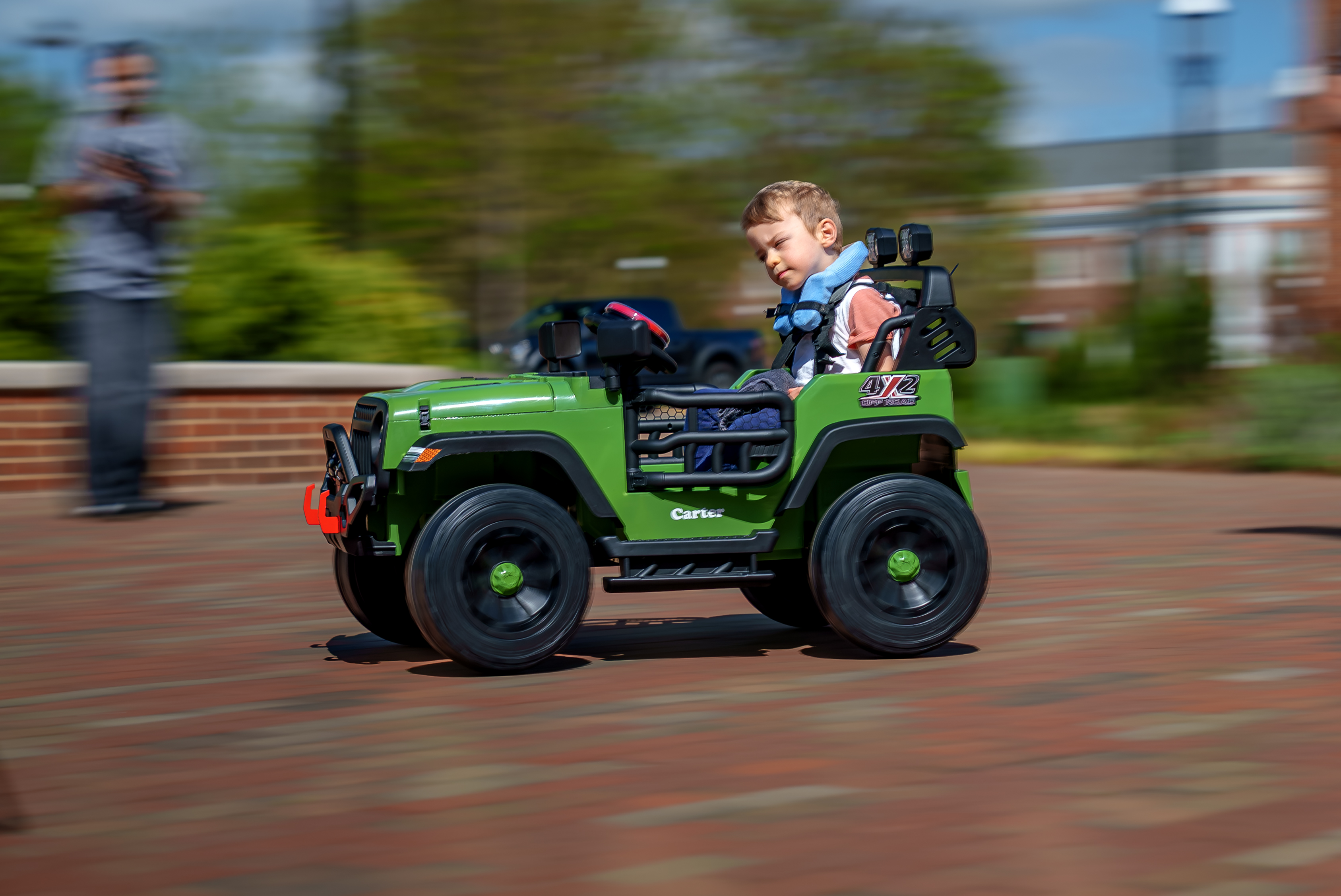 Child drives a green ride-on toy car outdoors with motion blur showing movement.
