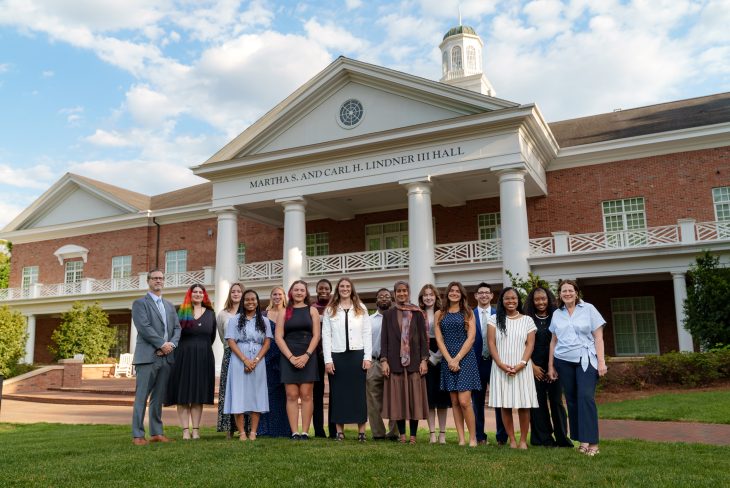 A group of people pose in front of a university building with white columns and brick facade