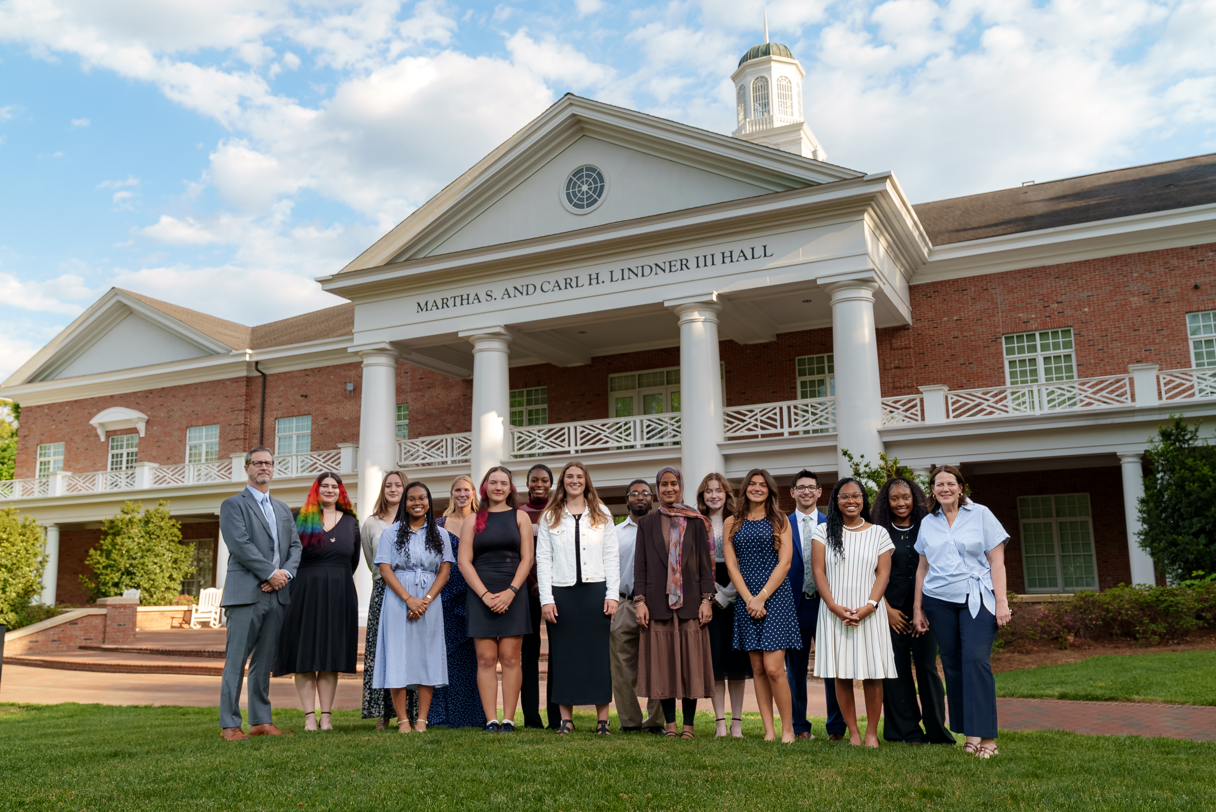 A group of people pose in front of a university building with white columns and brick facade