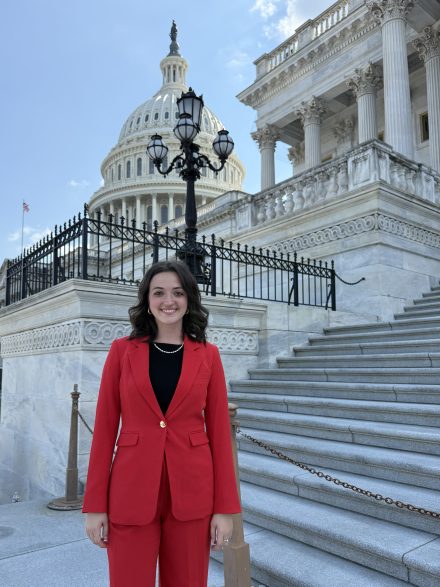 Maddie Hewgley wearing a red blazer and red dress pants standing in front of the U.S. Capitol.