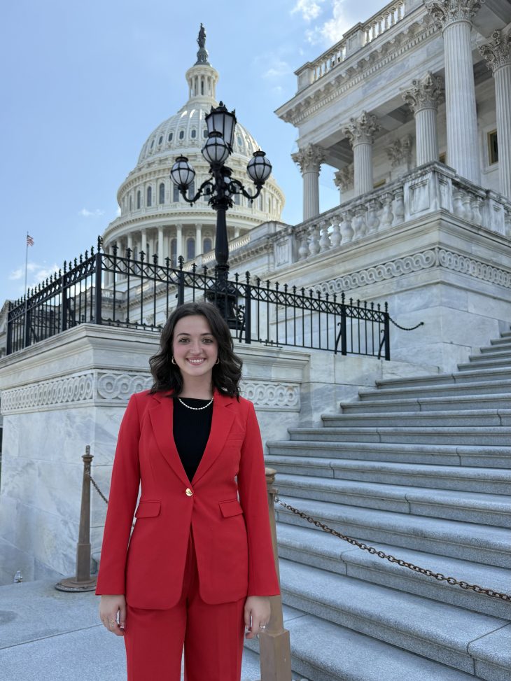 Maddie Hewgley wearing a red blazer and red dress pants standing in front of the U.S. Capitol.