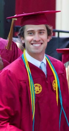 Doug Williams '13, wearing a cap and gown, seen smiling during his graduation ceremony from Elon.