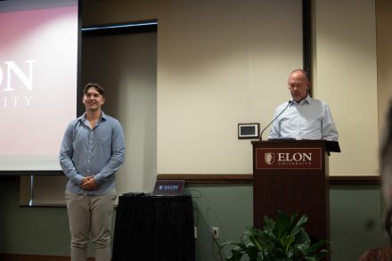 A presenter announces an award recipient during the ceremony as a student stands nearby, awaiting recognition for leadership and achievement.