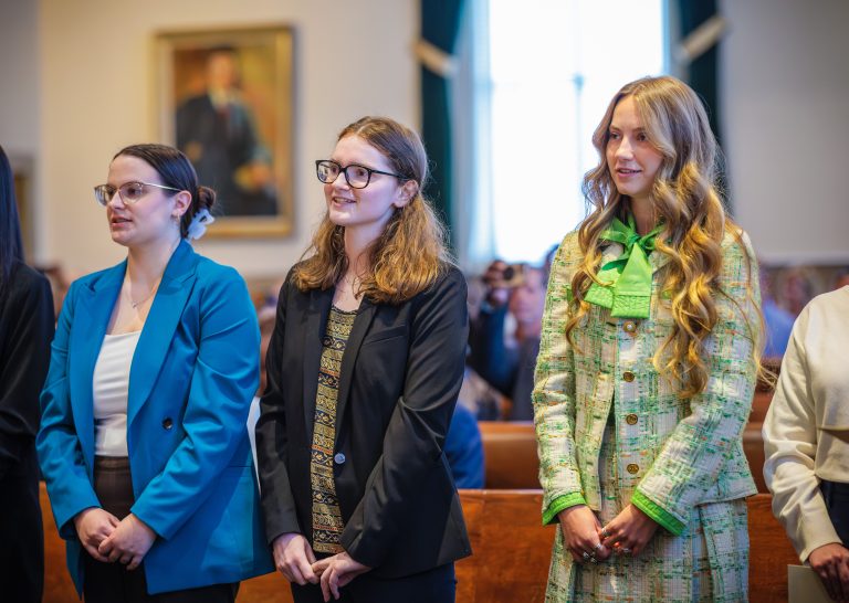 Three women stand, smiling, in front of a courtroom.