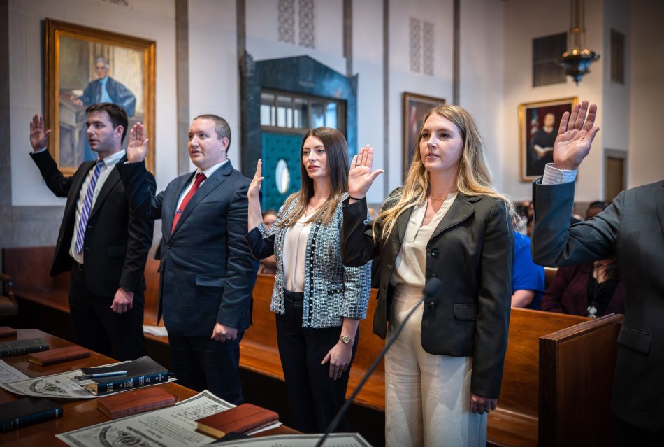Four people with right hands raised as they take an oath in a courtroom.
