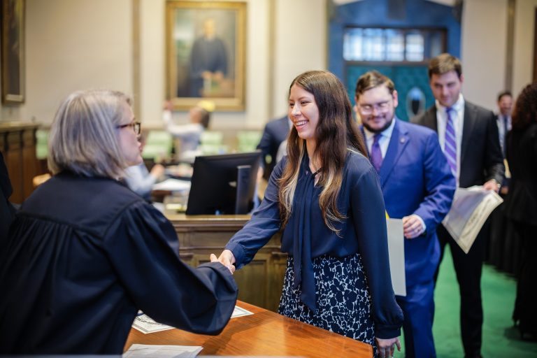 A woman in professional dress shakes hands with a female judge wearing a robe.