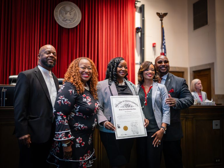A group of people stand in the front of a courtroom smiling fro a photo