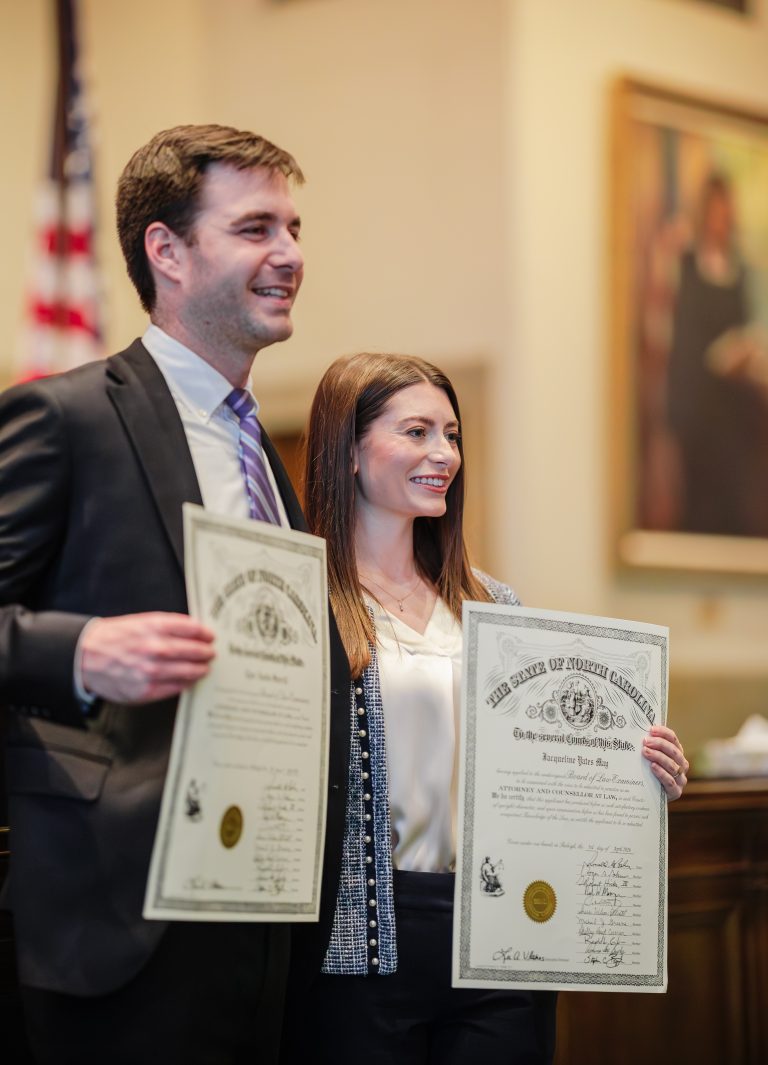 A man and a woman hold their law licenses smiling in a courtroom.