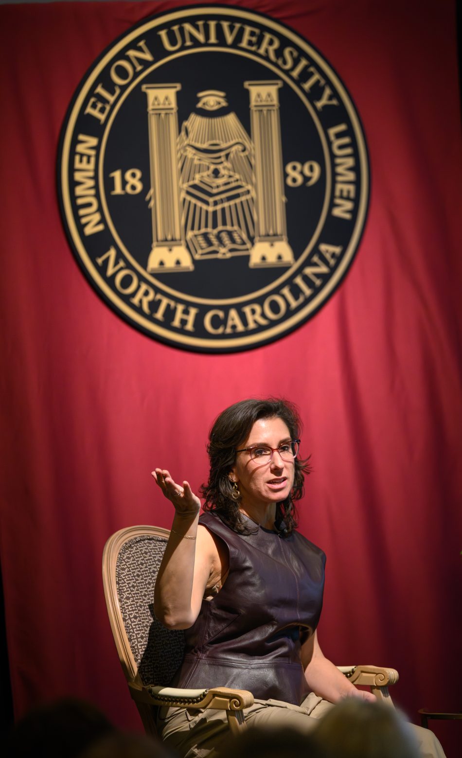 Jodi Kantor speaks on a stage with a maroon backdrop and Elon University seal behind her