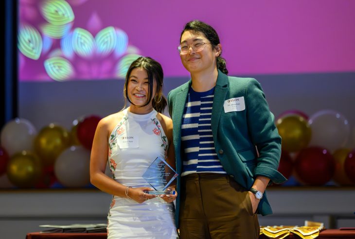 Student and faculty member pose together on stage during an awards celebration, with one student holding an award.